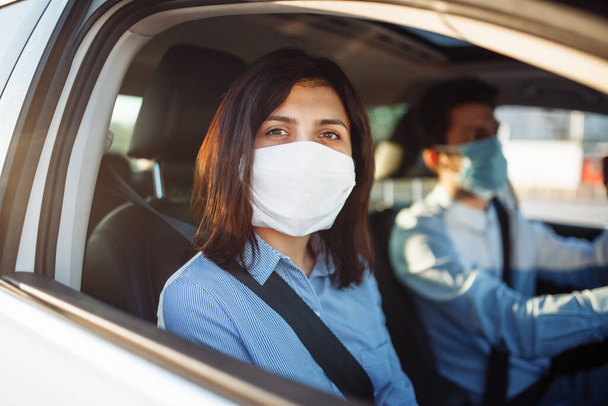 Genç kız yolcu, koronavirüs salgını karantinası sırasında taksiyle gezintiye çıkıyor. Kadının biri steril tıbbi maske takarak arabanın camından dışarı bakıyor. Sosyal uzaklık ve sağlık güvenliği kavramı - Fotoğraf, Görsel