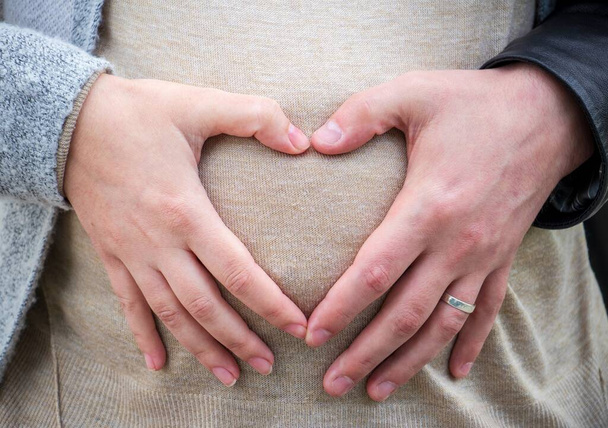The parents forming a heart on the belly of a pregnant female - parenthood concept - Foto, Imagen