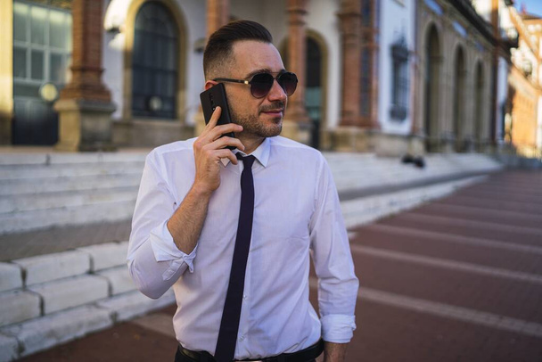 Успішний молодий бізнесмен в офіційному вбранні з сонцезахисними окулярами, що розмовляють по телефону
 - Фото, зображення