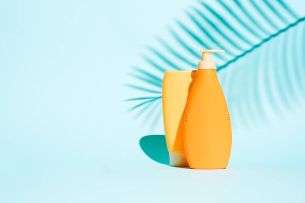 Orange containers for lotion without label on blue background with leaf - Фото, зображення