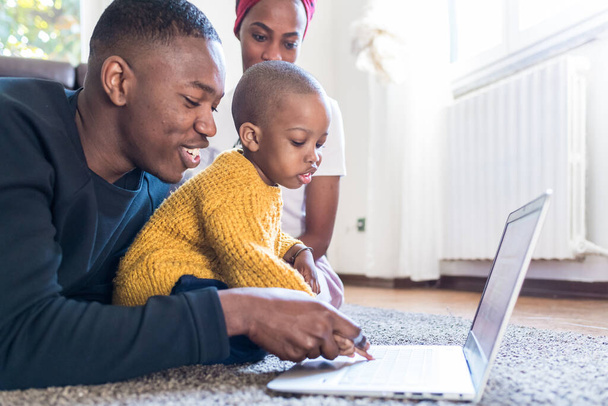 ευτυχισμένη οικογένεια εσωτερική με το παιδί χρησιμοποιώντας φορητό υπολογιστή - ψυχαγωγία, μάθηση, έννοια της τεχνολογίας - Φωτογραφία, εικόνα
