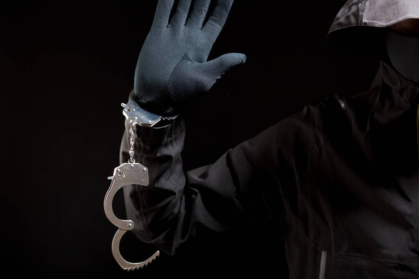 primer plano de las manos de un ladrón en guantes negros con esposas sobre un fondo negro. - Foto, imagen
