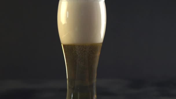 Beer is pouring into a glass. Beer forming waves close up. Pouring beer into glass with bubbles close up. Beer is pouring from the top into the glass forming a foam and spills out . Slow motion - Filmagem, Vídeo