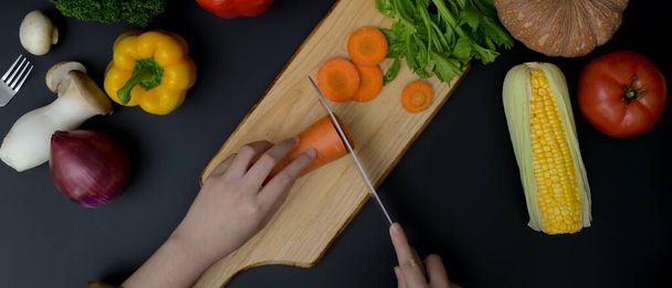 Overhead shot de cocinera cortando zanahoria fresca en el bloque de picado en la cocina moderna oscura
  - Foto, imagen