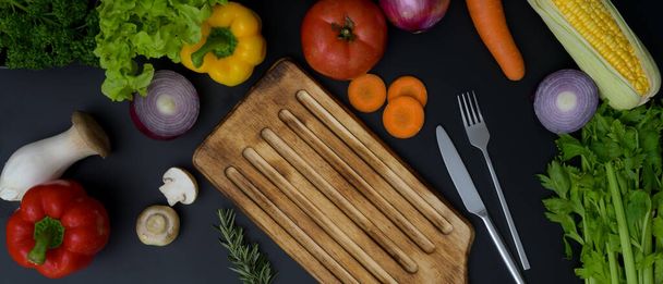 Vue de dessus de la table de cuisine sombre avec assortiment de légumes frais, planche à découper et argenterie  - Photo, image