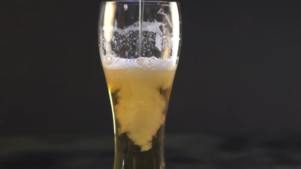 Beer is pouring into a glass. Beer forming waves close up. Pouring beer into glass with bubbles close up. Beer is pouring from the top into the glass forming a foam and spills out . Slow motion - Πλάνα, βίντεο