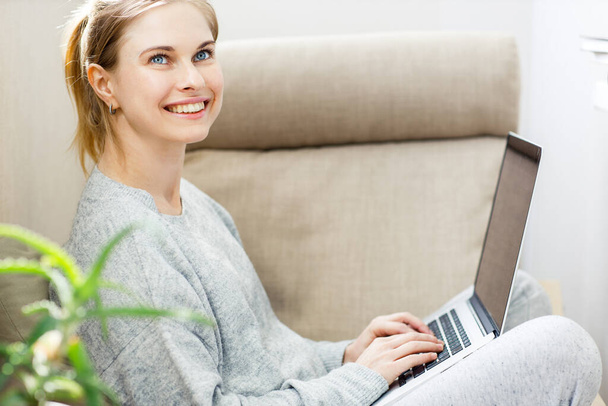 Loira feliz em terno caseiro cinza com laptop em suas mãos sentado na cadeira
 - Foto, Imagem