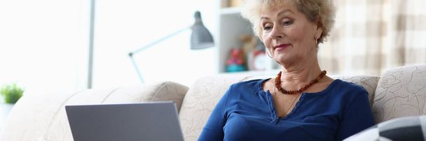 Femme âgée assise avec un ordinateur portable sur son genou maison
 - Photo, image