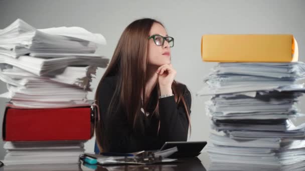 A pile of unfinished documents and paperworks at the table, colorful folders and pensive female accountant in glasses. Business worker thinking about calculations and financial reports. Analytics - Footage, Video