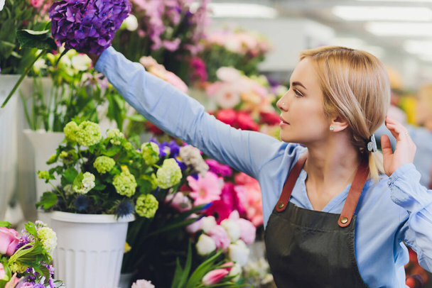 Female sales assistant working as florist and holding bouquet with customer in background. Horizontal shape, waist up. - Photo, Image