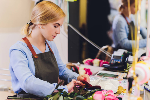 Female sales assistant working as florist and holding bouquet with customer in background. Horizontal shape, waist up. - Фото, зображення