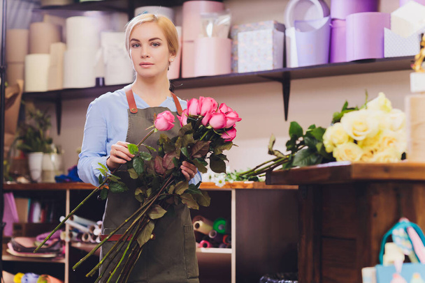 Female sales assistant working as florist and holding bouquet with customer in background. Horizontal shape, waist up. - Foto, Imagem