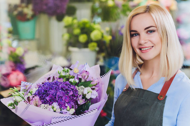 Female sales assistant working as florist and holding bouquet with customer in background. Horizontal shape, waist up. - 写真・画像