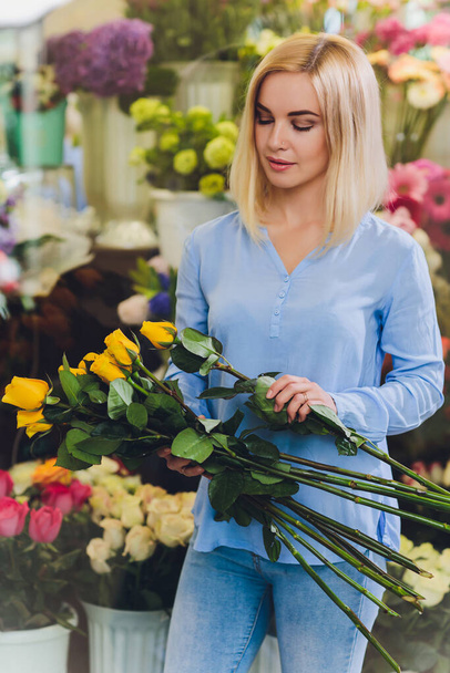 Female sales assistant working as florist and holding bouquet with customer in background. Horizontal shape, waist up. - Φωτογραφία, εικόνα