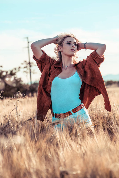 beautiful blonde girl in wheat field with white shirt and reindeer country jacket at sunset. High quality photo - 写真・画像