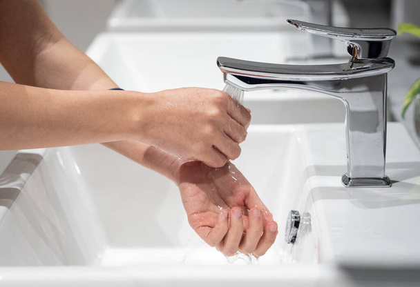 公共のバスルームで蛇口に手を洗う若い女性の閉じる。コロナウイルスパンデミックからの安全予防対策のための手洗いジェスチャー. - 写真・画像