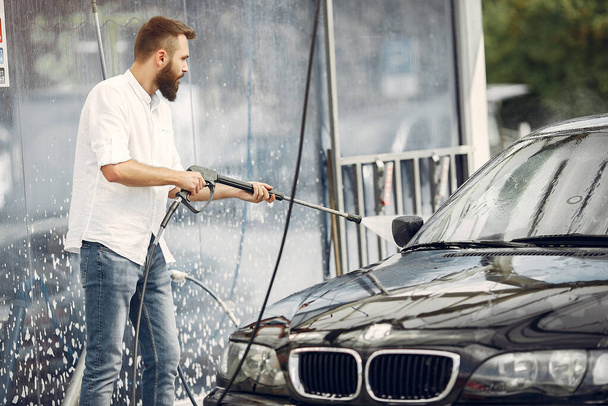 Handsomen man in a white shirt washing his car - Фото, зображення