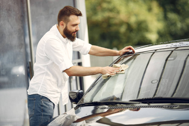Man in a white shirt wipes a car in a car wash - Fotó, kép