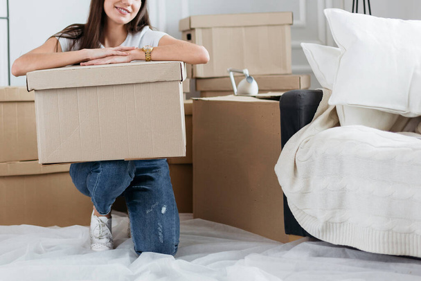 young woman with a cardboard box sitting on the floor in a new apartment - Foto, Imagem