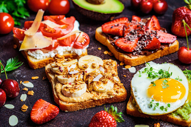 Desayuno diferentes tostadas con bayas, queso, huevo y fruta, fondo oscuro
. - Foto, Imagen