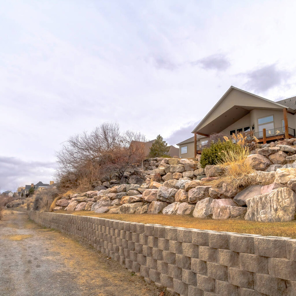 Plac upraw Brudna droga wzdłuż domów na stoku z ogromnymi skałami i betonową ścianą oporową - Zdjęcie, obraz