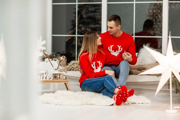 Фото влюбленной пары в уютной комнате, обнимающей новогоднюю гирлянду фонарей. Улыбающаяся женщина обнимает своего парня на День Святого Валентина. - Фото, изображение