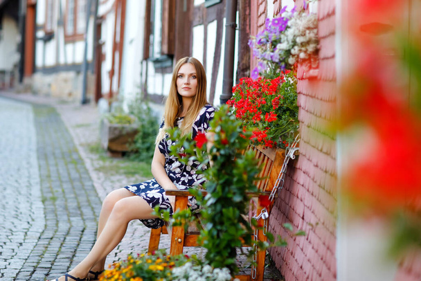Красивая молодая женщина с длинными волосами в летнем платье отправляется на прогулку по немецкому городу. Счастливая девушка с удовольствием гуляет по симпатичному городку со старыми домами в Германии. - Фото, изображение