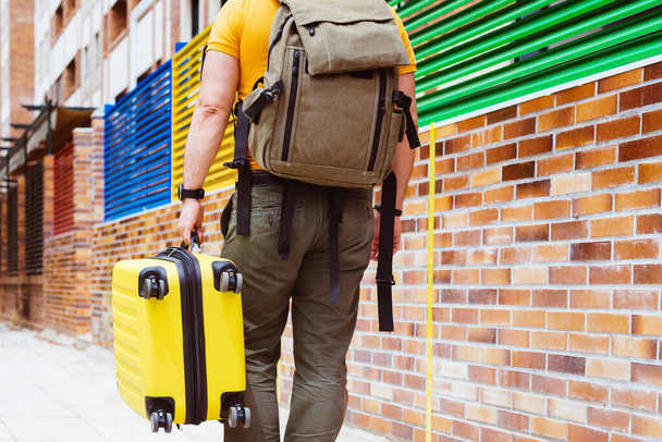 Sarı bir bavul ve sırt çantasıyla dolaşan bir adam. - Fotoğraf, Görsel