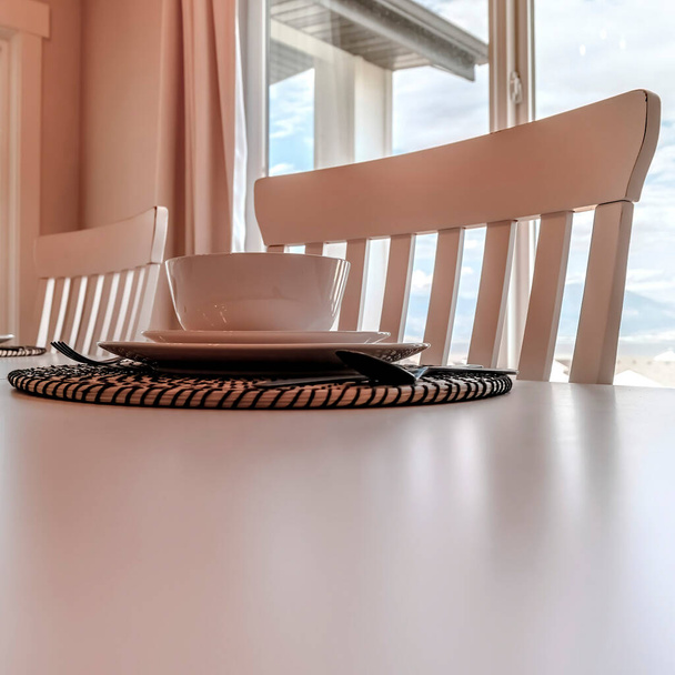 Kwadratowe uprawy Naczynia stołowe i naczynia na plecionej podkładce przy stole z krzesłami - Zdjęcie, obraz