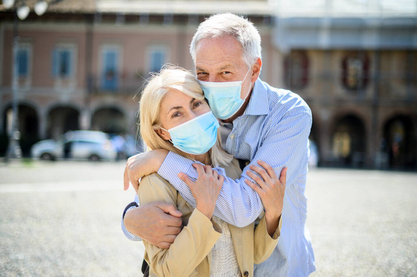 Love in the time of Coronavirus. Senior couple hugging outdoor wearing masks - Photo, image