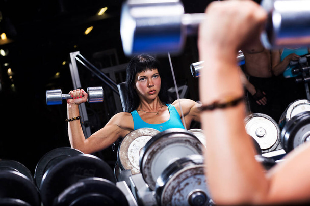 Beautiful muscular woman with dark hair is working out in a gym - Foto, Imagen