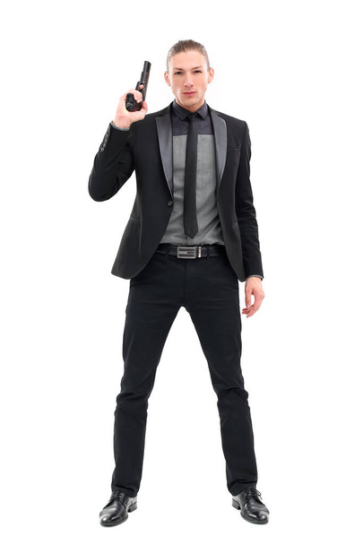 Schöner Mann in schwarzem Anzug und Pistole posiert vor weißem Hintergrund - Foto, Bild