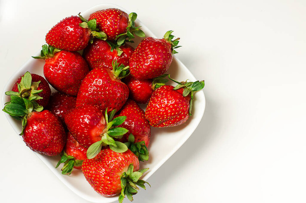 Fresh, juicy, sweet strawberries in a white plate stands on a white background. Natural vitamins. Useful sweets. Summer dessert. The concept of healthy eating. - Photo, Image