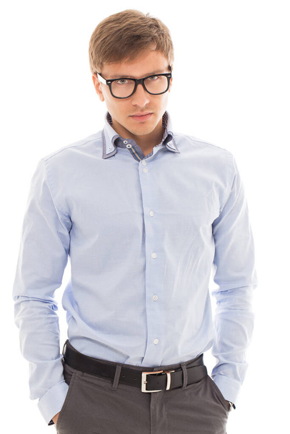 Handsome man in a blue shirt and glasses holds his hands in pockets over a white background - Foto, imagen
