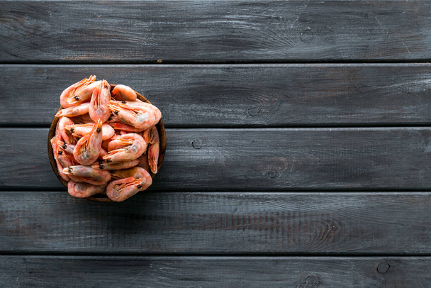 Shrimps in shell in bowl on dark wooden table top-down copy space - Foto, afbeelding