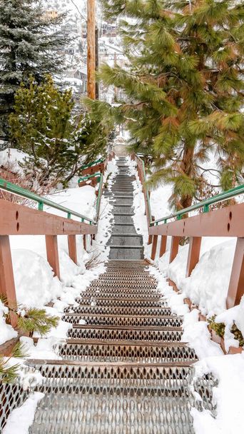 Vertical frame Stairway on hill overlooking rooftops homes and trees with fresh snow in winter - Photo, Image