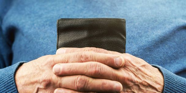 aged person in blue pullover hands hold small black wallet - 写真・画像