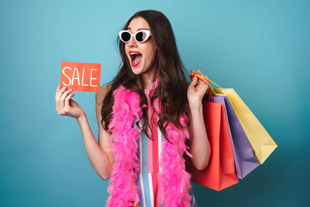 Image of delighted nice woman in boa holding sale card and shopping bags isolated over blue background - Foto, Bild