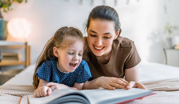 Счастливая семья. Милая молодая мать читает книгу своей дочери на кровати дома. - Фото, изображение