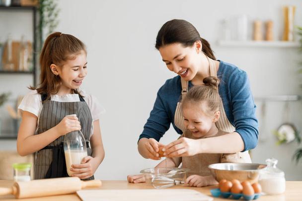 Happy loving family are preparing bakery together. Mother and children daughters girls are cooking cookies and having fun in the kitchen. Homemade food and little helper.  - Valokuva, kuva