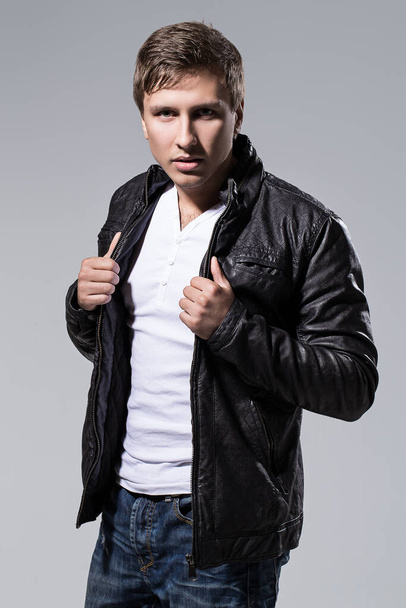 Handsome man in leather jacket, jeans and white t-shirt is posing over a grey background - Fotografie, Obrázek