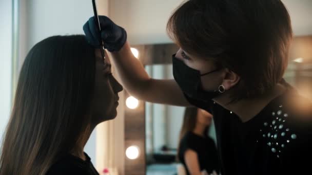 Une jeune femme cosmétologue dessine un marquage blanc sur les sourcils d'un mannequin - Séquence, vidéo