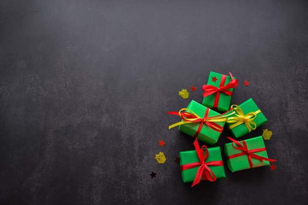 Cadeaus in groen papier met rode en gele linten liggen naast elkaar in de vorm van een kerstboom met daarop een rode ster. Zwarte achtergrond, kopieer ruimte. Groot verkoopconcept - Foto, afbeelding