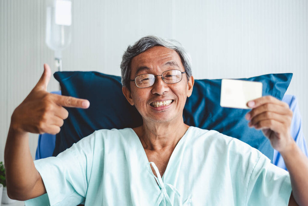 Viejo asiático paciente hombre mostrando tarjeta de crédito con feliz y sonrisa en paciente cama - Foto, imagen