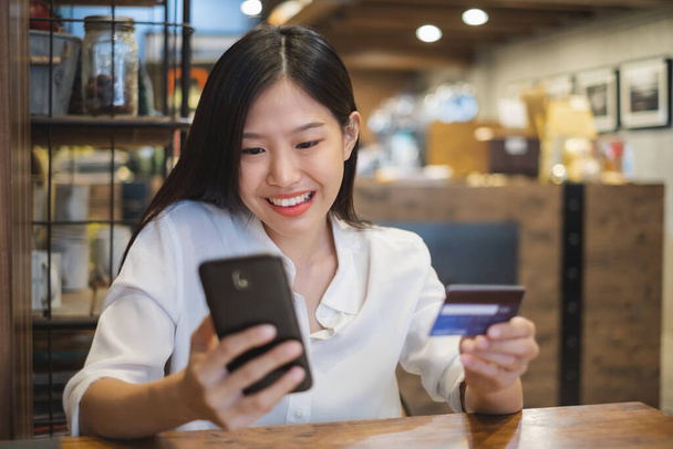 Jeune belle femme asiatique utilisant un téléphone intelligent et une carte de crédit pour faire du shopping en ligne dans un café-restaurant - Photo, image