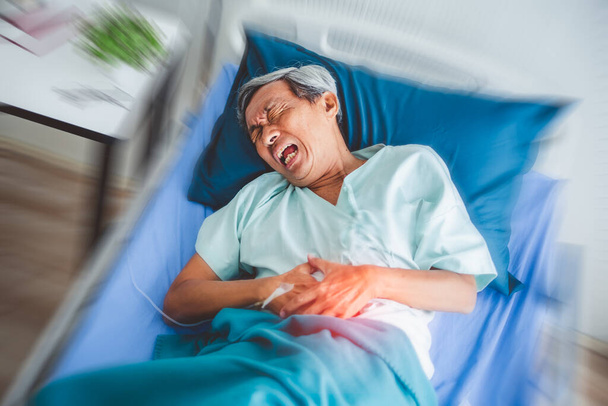 Vieux patient asiatique souffrant de maux d'estomac, douloureux couché sur le lit du patient à l'hôpital - Photo, image