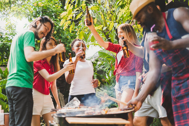Gruppo di persone diversificate che organizzano barbecue / barbecue a casa, cucinano carne / manzo alla griglia per pranzo, concetto di stile di vita felice per gli amici - Foto, immagini