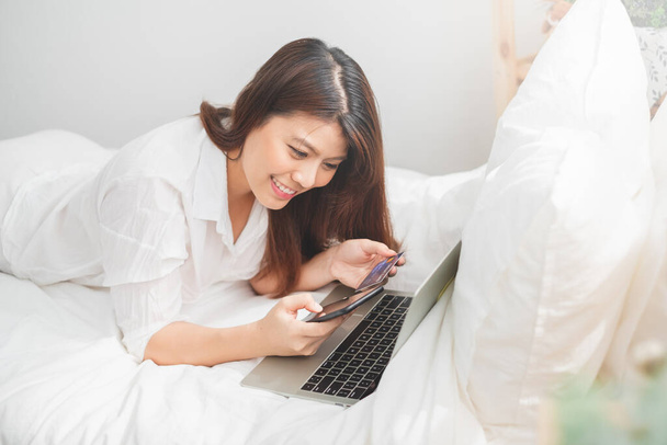 Gyönyörű ázsiai nő segítségével laptop és okostelefon a szobában az online vásárlás, ázsiai nő életmód koncepció - Fotó, kép