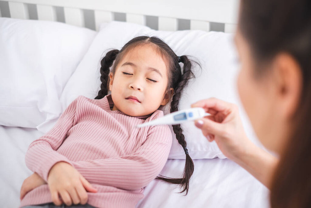 Mother using thermometer with her girl kid daughter for sickness and fever - Foto, immagini