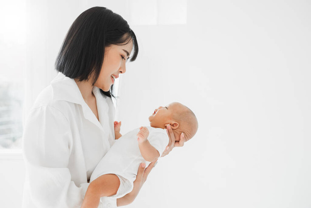 Junge asiatische Mutter hält ihr Neugeborenes liebevoll auf weißem Bett, Muttertagskonzept - Foto, Bild